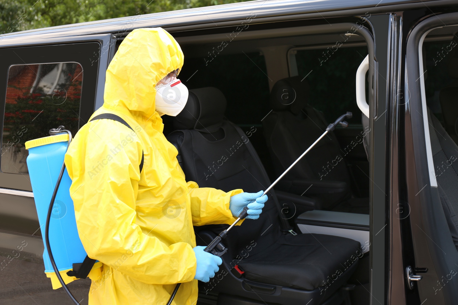 Photo of Person in protective suit disinfecting car with sprayer. Preventive measure during coronavirus pandemic