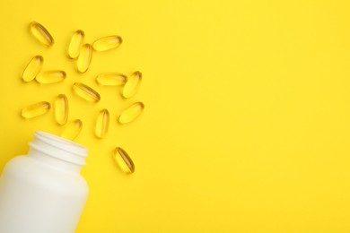 Photo of Softgel capsules and bottle on yellow background, top view. Space for text