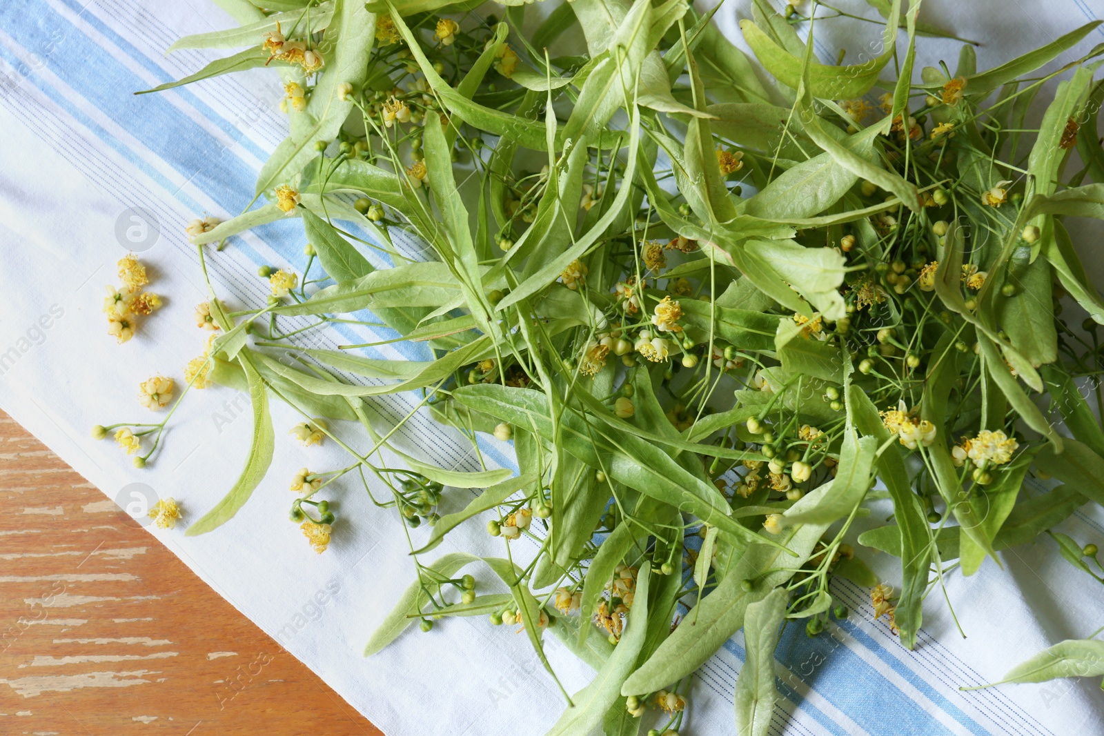 Photo of Pile of beautiful linden blossoms and green leaves on wooden table, top view