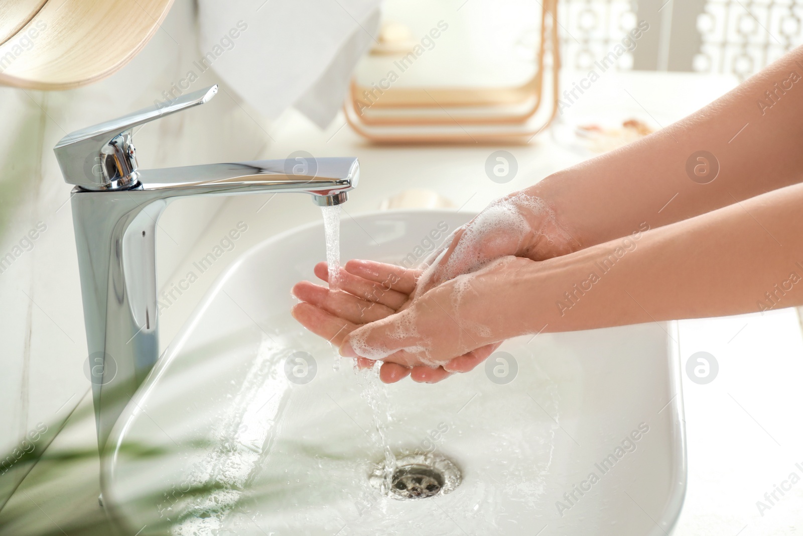 Photo of Young woman washing hands with soap over sink in bathroom, closeup