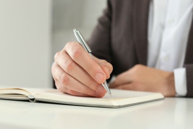 Photo of Man writing in notebook at white table, closeup