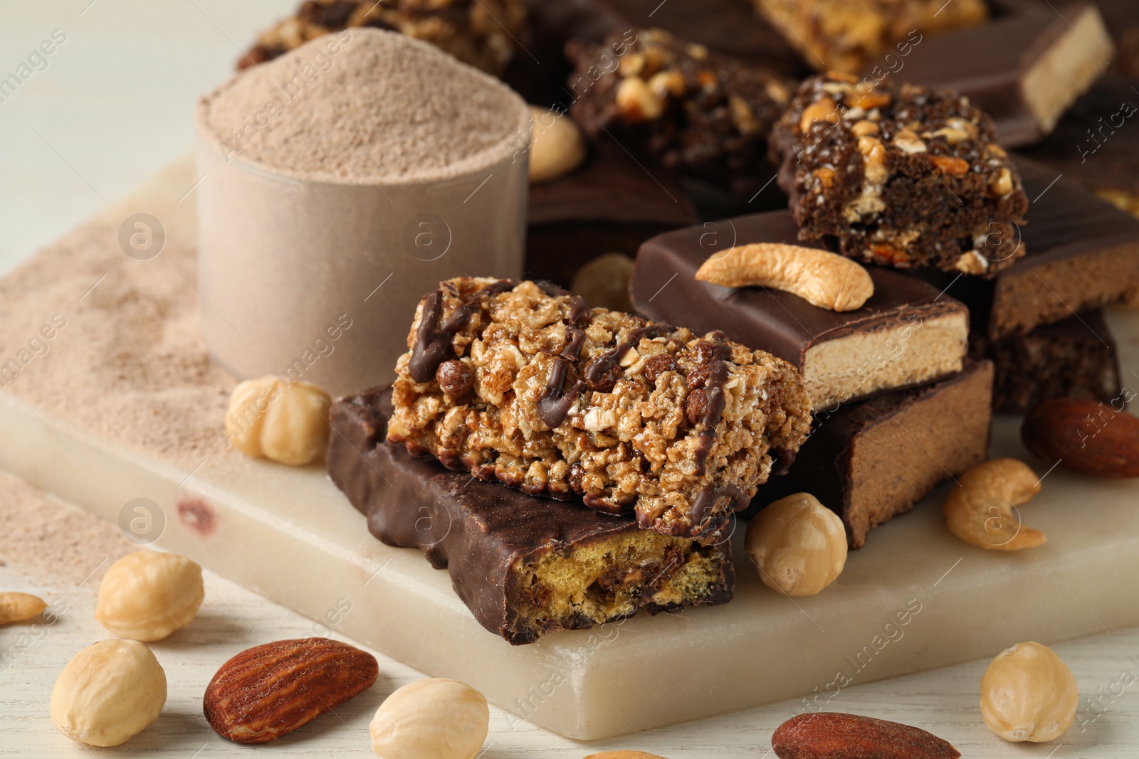 Photo of Different tasty energy bars, nuts and protein powder on white table, closeup