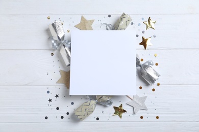 Photo of Flat lay composition of Christmas crackers, shiny confetti and blank paper on white wooden background. Space for text