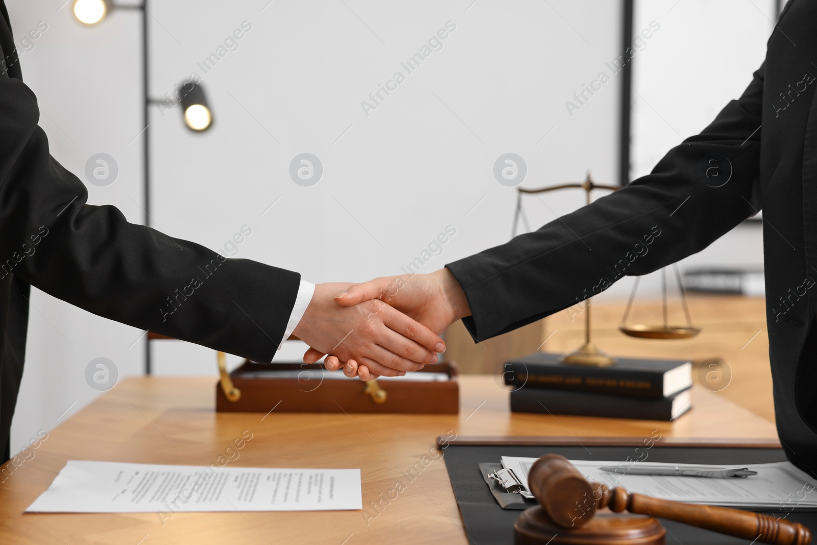 Photo of Notary shaking hands with client at wooden table in office, closeup