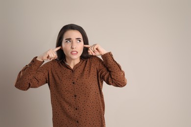 Photo of Emotional young woman covering ears with fingers on beige background, space for text