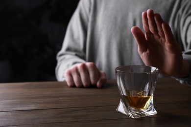 Photo of Man refusing to drink whiskey at wooden table, closeup. Alcohol addiction