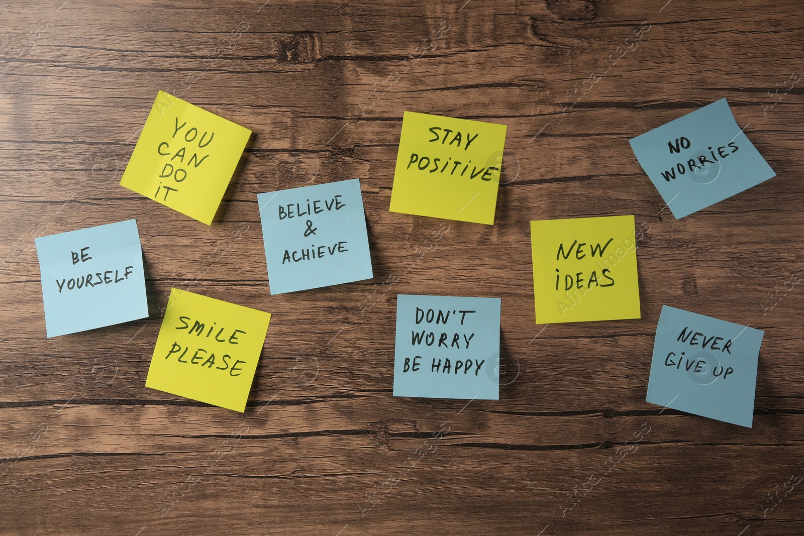 Photo of Paper notes with life-affirming phrases on wooden table, flat lay