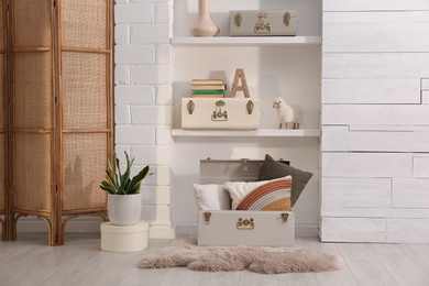Photo of Stylish storage trunks, plant and different decor elements near white wall indoors. Interior design