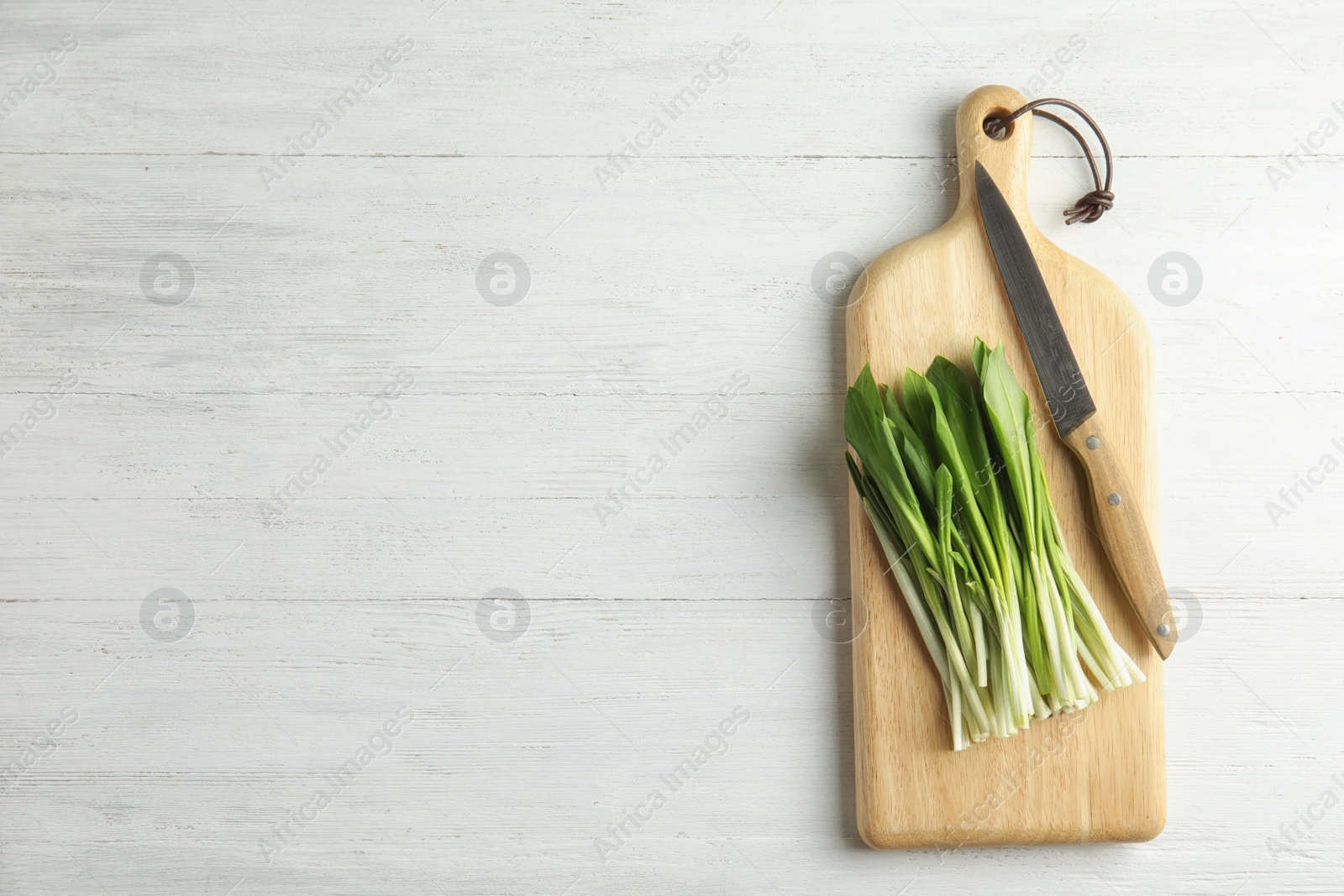 Photo of Board with wild garlic or ramson and knife on white wooden table, top view. Space for text