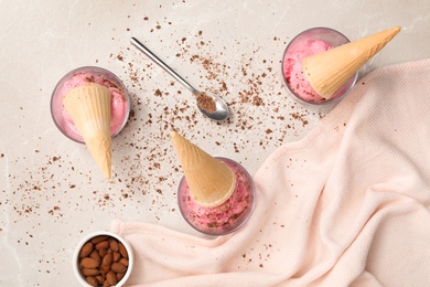 Photo of Flat lay composition with delicious pink ice cream in wafer cones, chocolate and almonds on light table