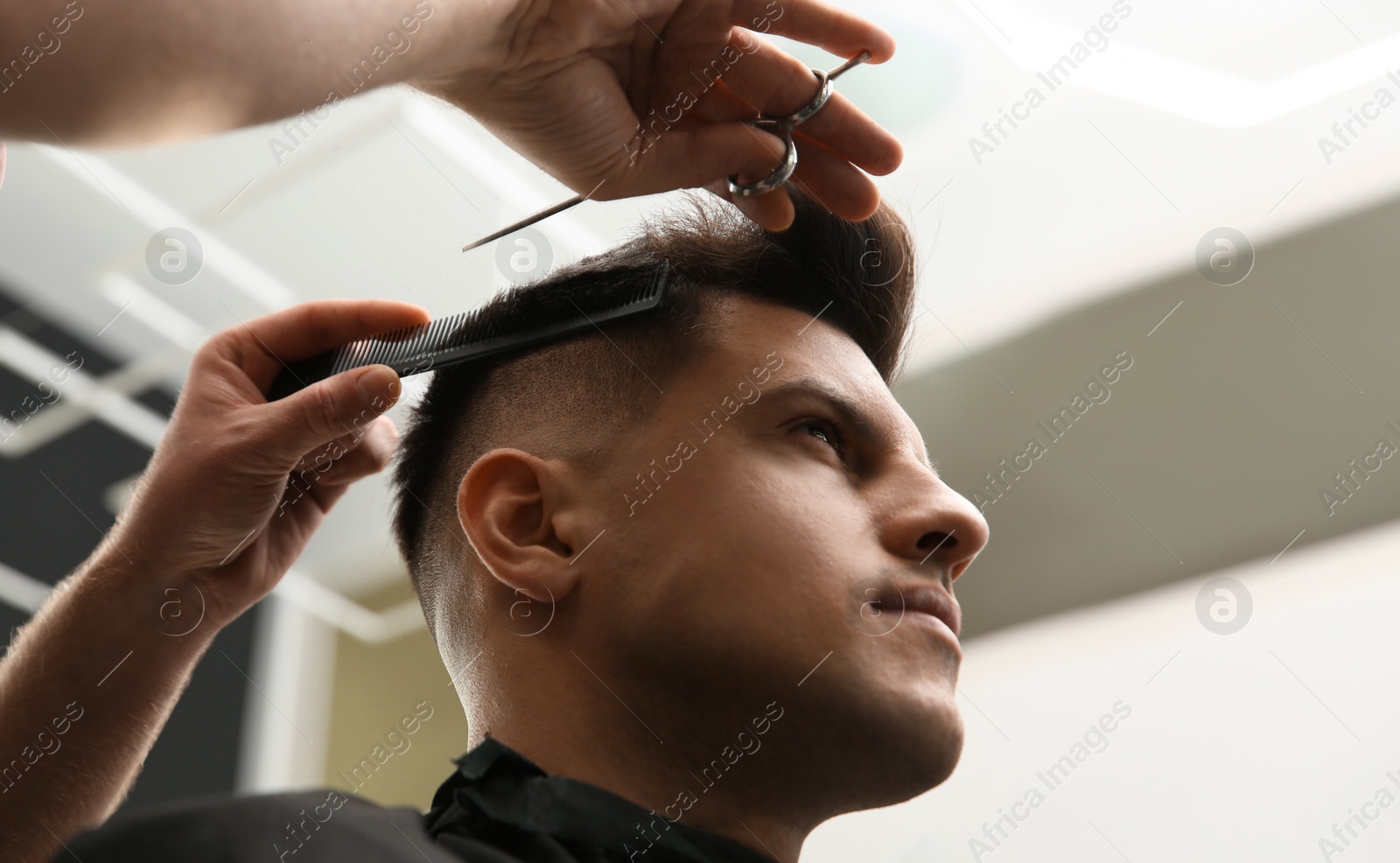 Photo of Professional barber making stylish haircut in salon, closeup