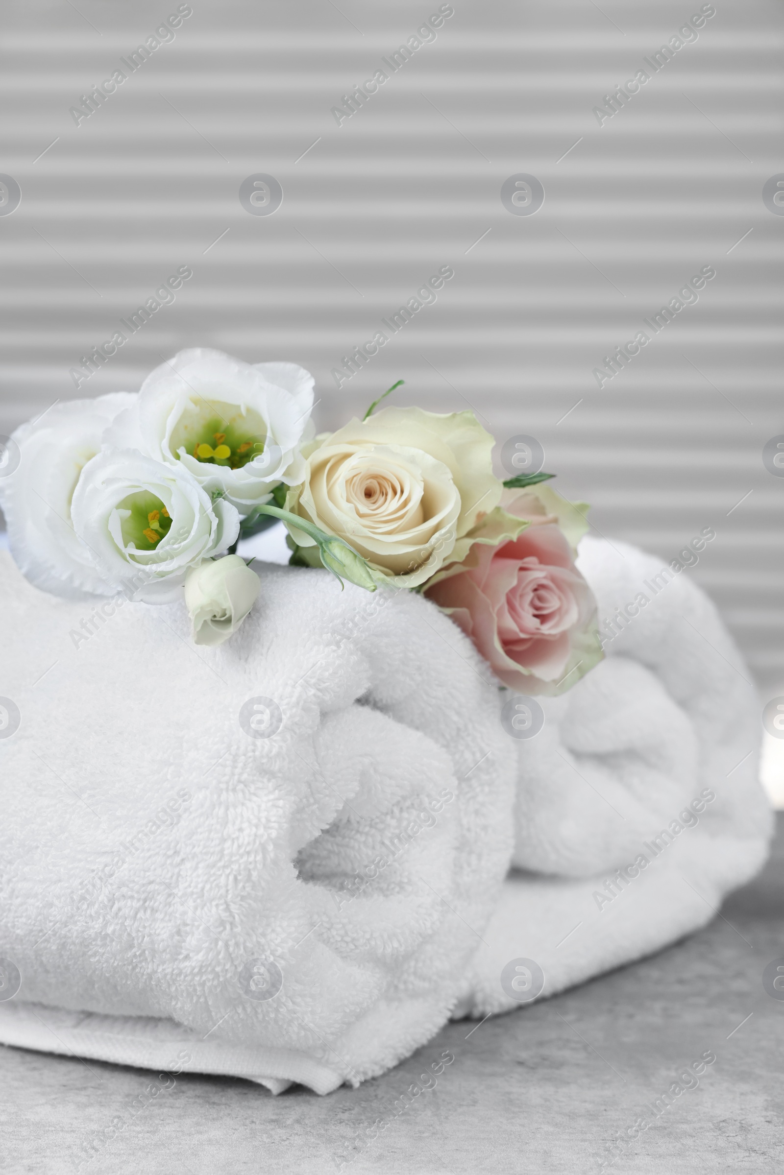 Photo of Rolled towels and flowers on grey table indoors