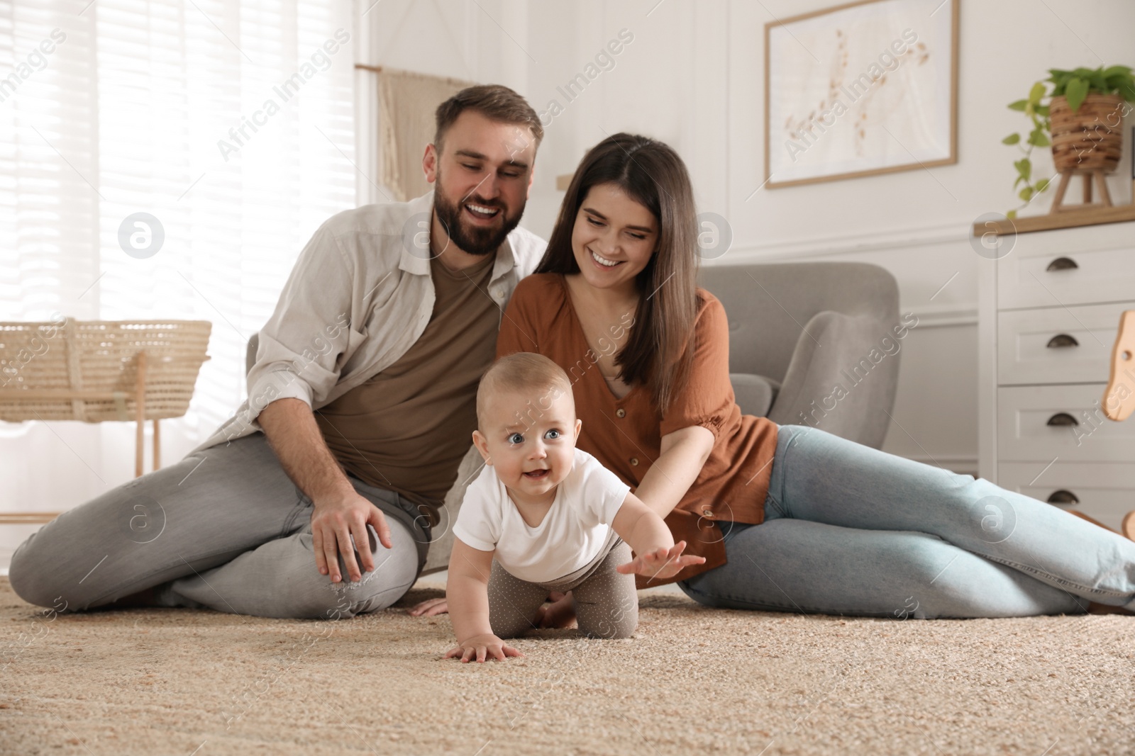 Photo of Happy parents watching their baby crawl on floor at home