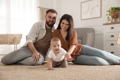 Photo of Happy parents watching their baby crawl on floor at home