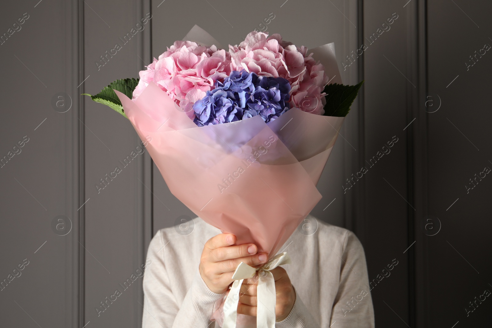 Photo of Woman with bouquet of beautiful hortensia flowers near grey wall