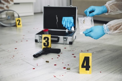 Investigator in protective gloves working with evidence indoors, closeup. Crime scene