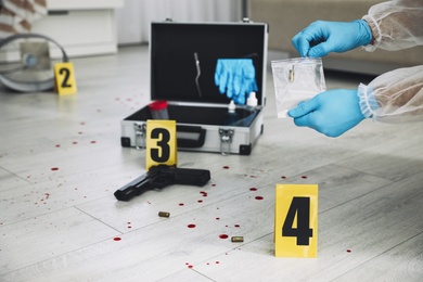 Photo of Investigator in protective gloves working with evidence indoors, closeup. Crime scene