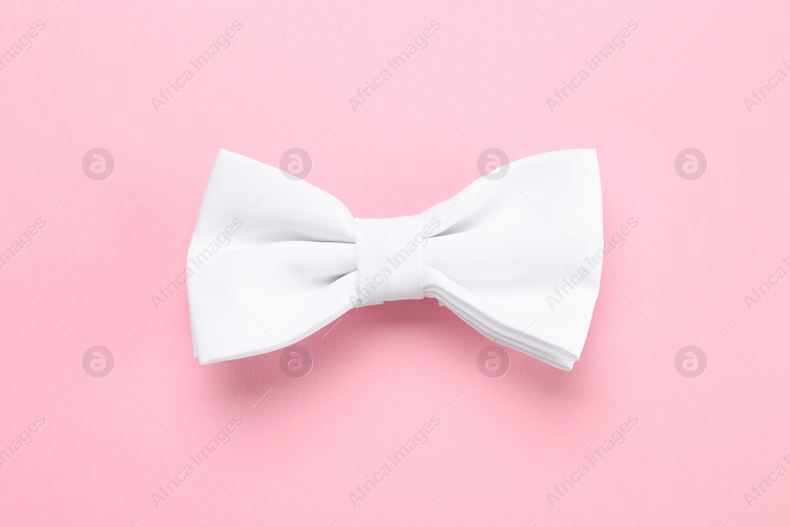 Photo of Stylish white bow tie on pink background, top view