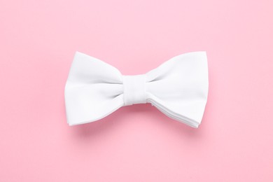 Photo of Stylish white bow tie on pink background, top view