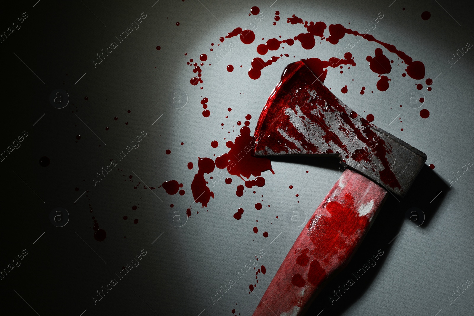 Photo of Axe with blood on gray surface in darkness, top view. Space for text