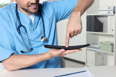 Photo of Male orthopedist showing insole in hospital, closeup