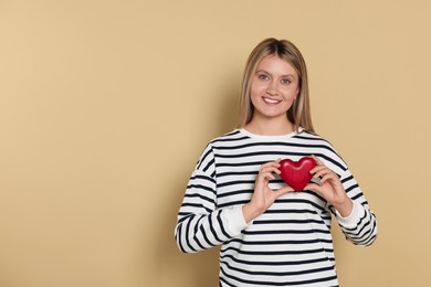 Happy volunteer holding red heart with hands on beige background. Space for text