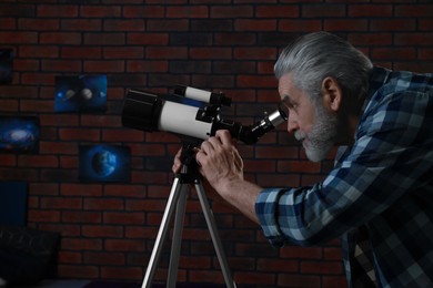 Senior man looking at stars through telescope in room