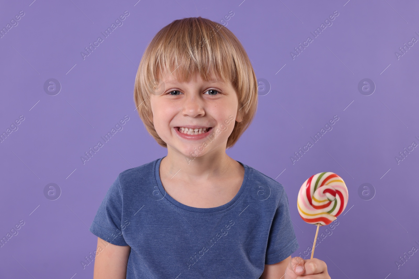 Photo of Happy little boy with colorful lollipop swirl on violet background