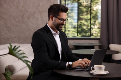 Happy young man with glasses working on laptop at table in office