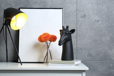 Photo of Stylish decor, vase with flowers, picture and desk lamp on white table near grey wall indoors, space for text. Interior design