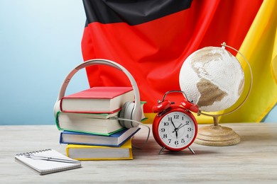 Photo of Learning foreign language. Different books, headphones, alarm clock and stationery on wooden table near flag of Germany