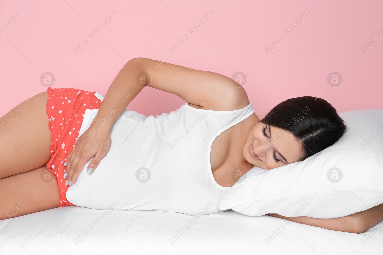 Photo of Beautiful pregnant woman lying with comfortable pillow on bed against color background