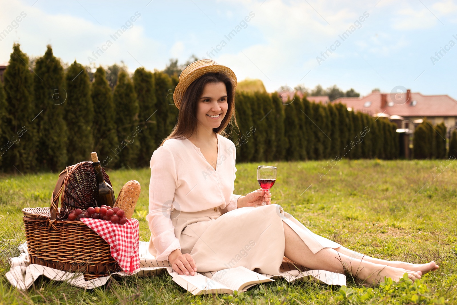 Photo of Happy woman with glass of wine reading book in park. Picnic season