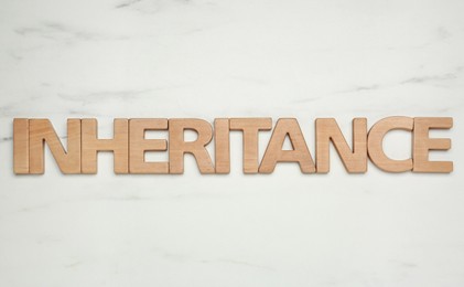 Photo of Word Inheritance made with wooden letters on white marble background, flat lay