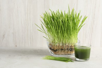 Photo of Wheat grass drink in glass and fresh sprouts on light table, space for text