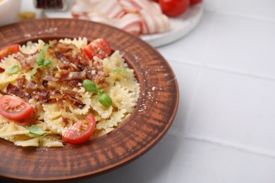 Tasty pasta with bacon, tomatoes and basil on white tiled table, space for text