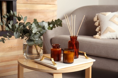 Photo of Eucalyptus branches, aromatic reed air freshener and candles on wooden table in living room. Interior element