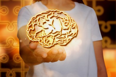 Image of Memory. Woman holding illustration of brain against puzzle pieces background, closeup