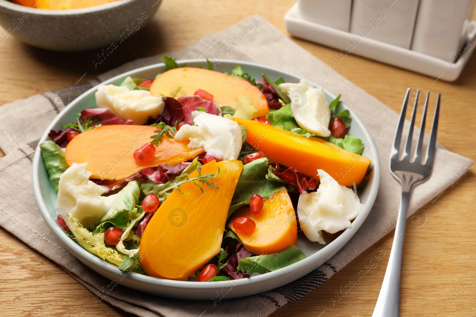 Photo of Delicious persimmon salad with cheese and pomegranate served on wooden table