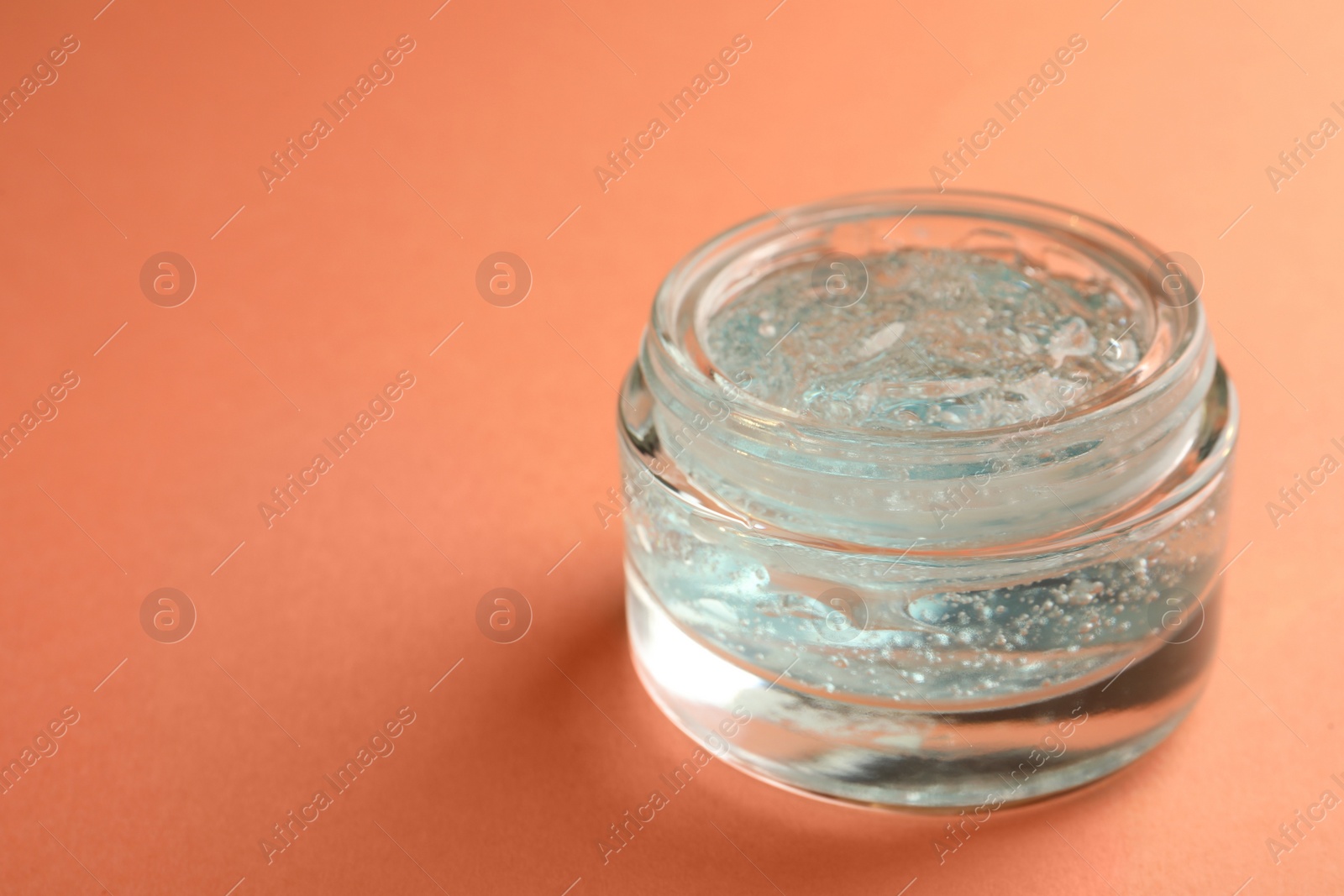 Photo of Jar of cosmetic gel on pale orange background, space for text