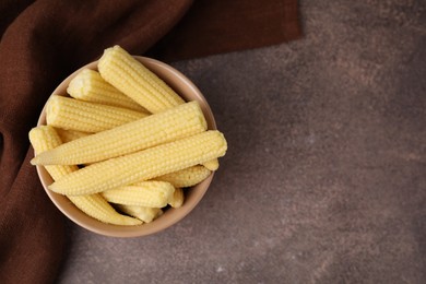 Photo of Tasty fresh yellow baby corns in bowl on brown table, top view. Space for text