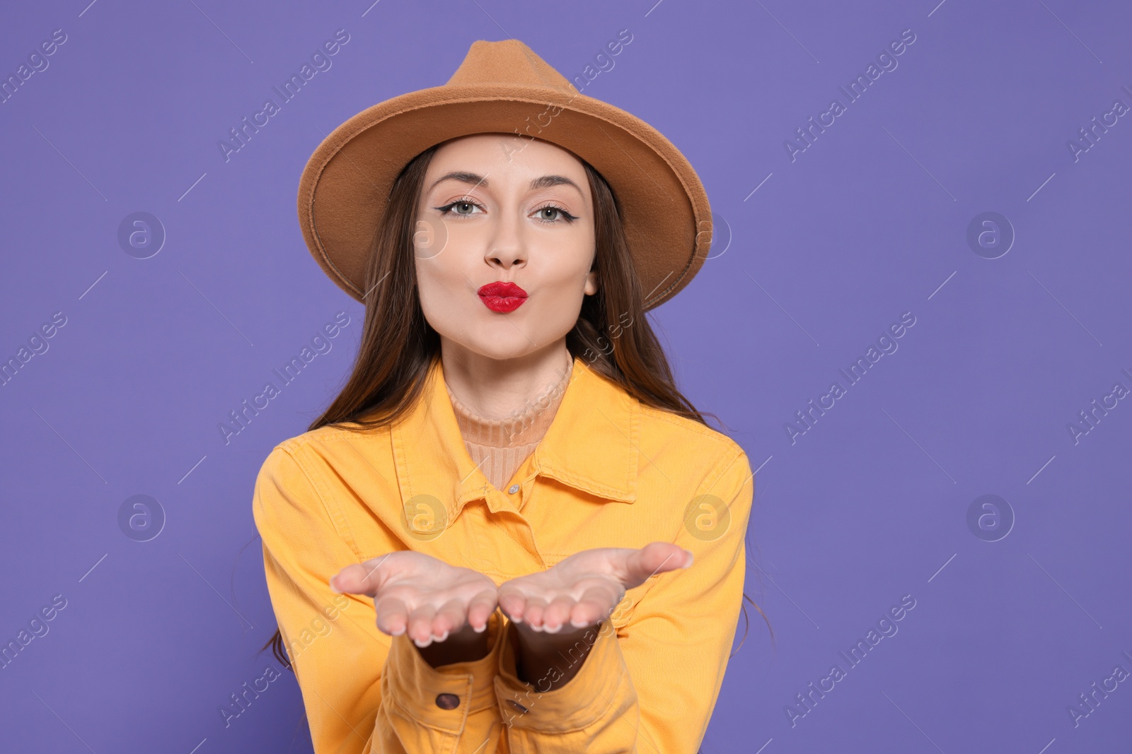 Photo of Beautiful young woman blowing kiss on purple background