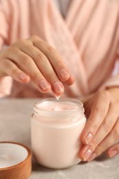 Photo of Woman applying hand cream at grey table, closeup