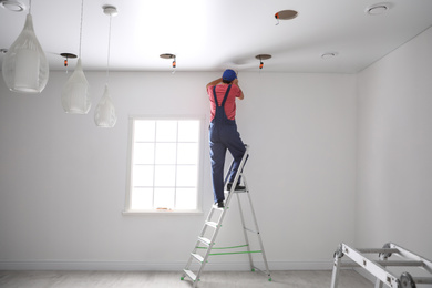 Photo of Worker installing stretch ceiling in empty room
