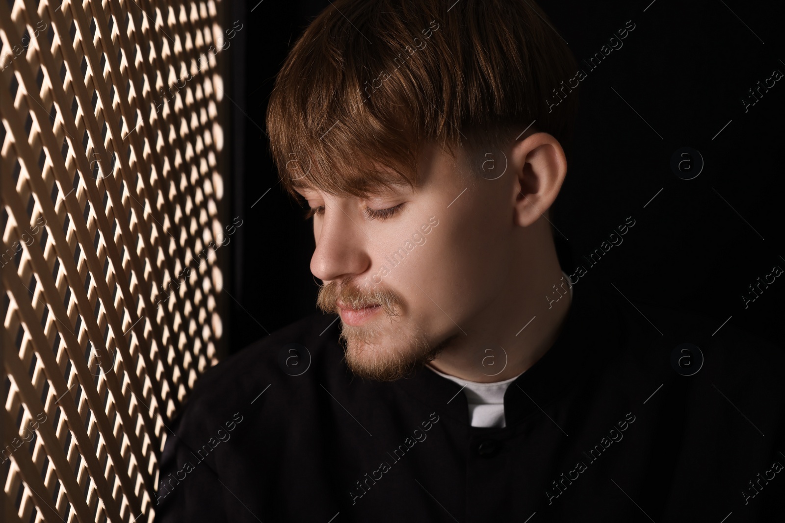Photo of Catholic priest near wooden window in confessional booth