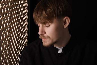 Photo of Catholic priest near wooden window in confessional booth