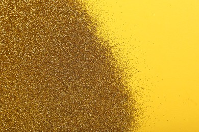 Photo of Shiny golden glitter on yellow background, top view. Space for text