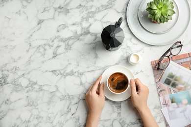 Young woman with cup of delicious hot coffee at table, top view