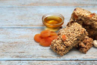 Photo of Tasty granola bars and ingredients on light blue wooden table. Space for text