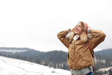 Young woman in warm clothes near snowy hill, space for text. Winter vacation